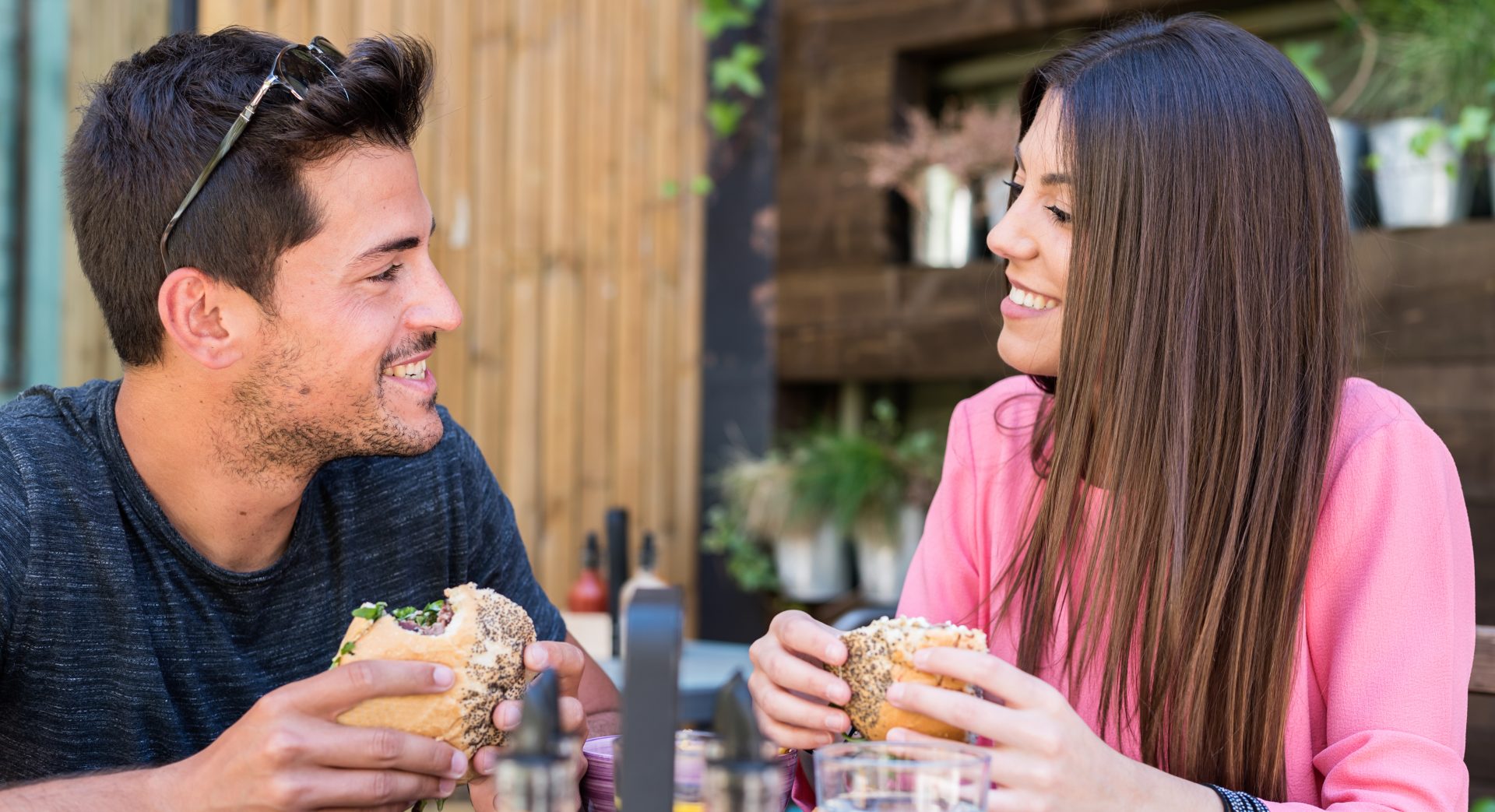 Happy young couple seating in a restaurant terrace eating a burger