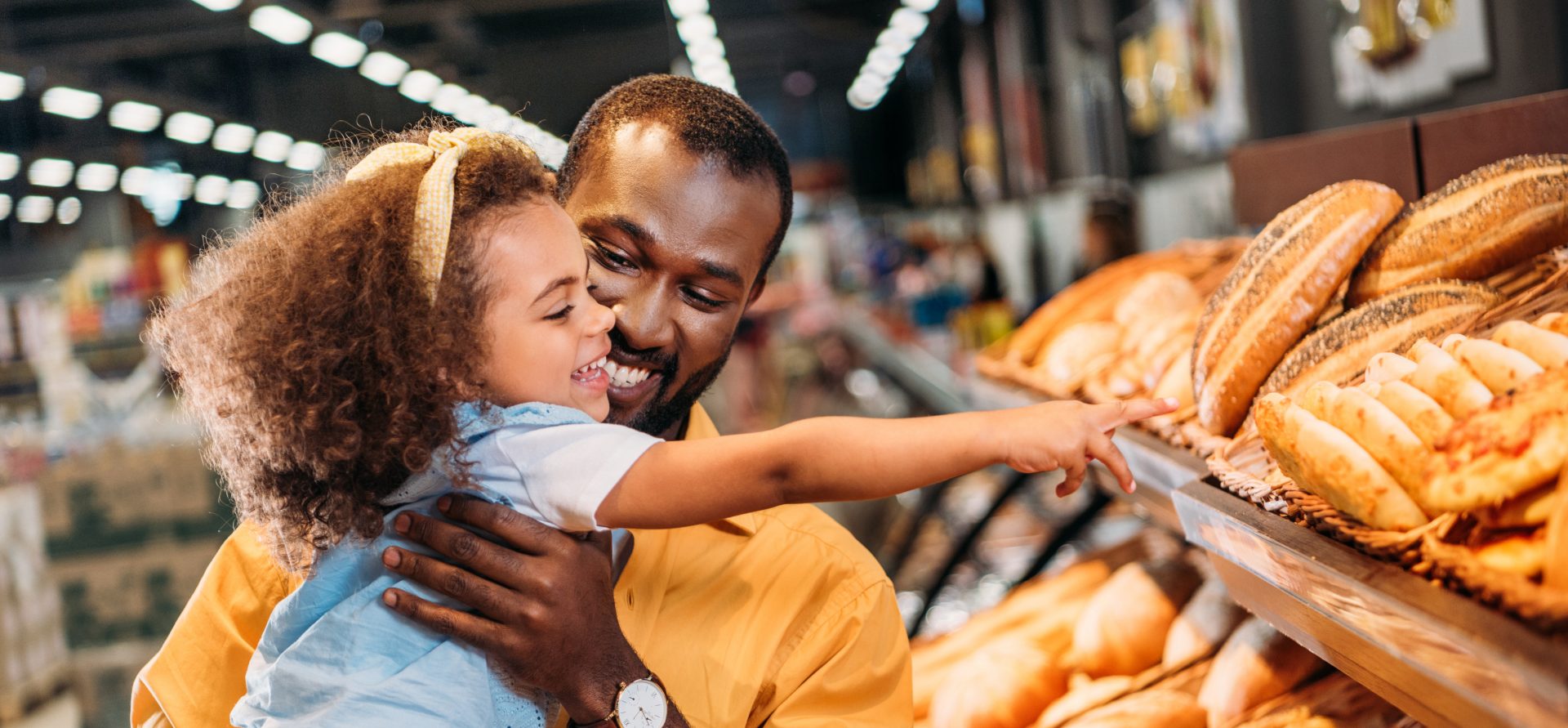 little child pointing by finger at pastry to father in supermarket
